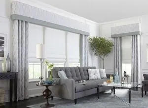 White Roman shades, box valances and patterned drapes in a grey living room