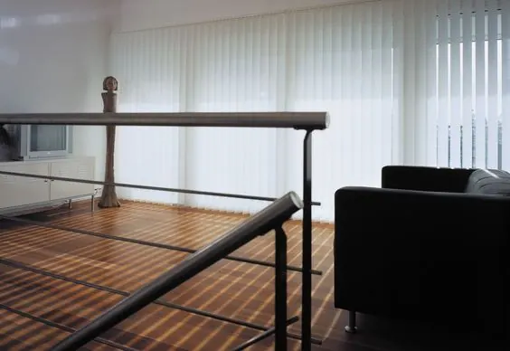 Stores verticaux blancs sur mezzanine avec garde-corps et fauteuil noir