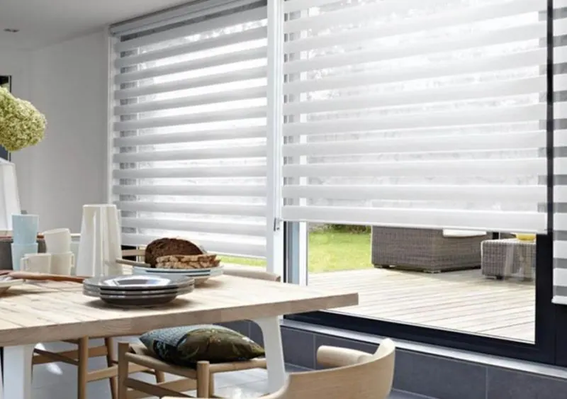 Store zébré blanc à demi baissé sur une porte-patio, table dressée