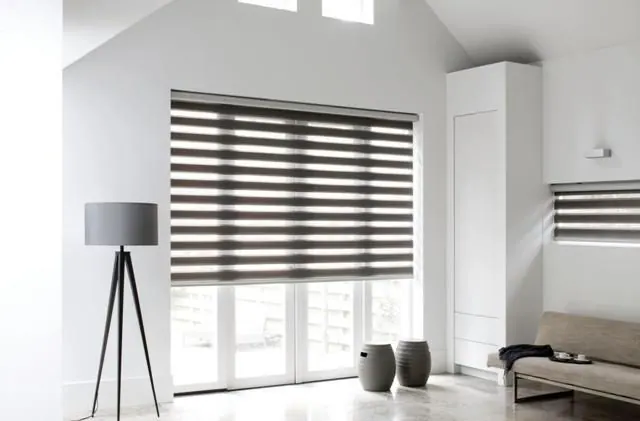 Store zébré gris foncé sur baie vitrée, salon blanc et lampe trépied