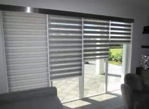 Stores alternés gris devant une porte coulissante, patio ensoleillé