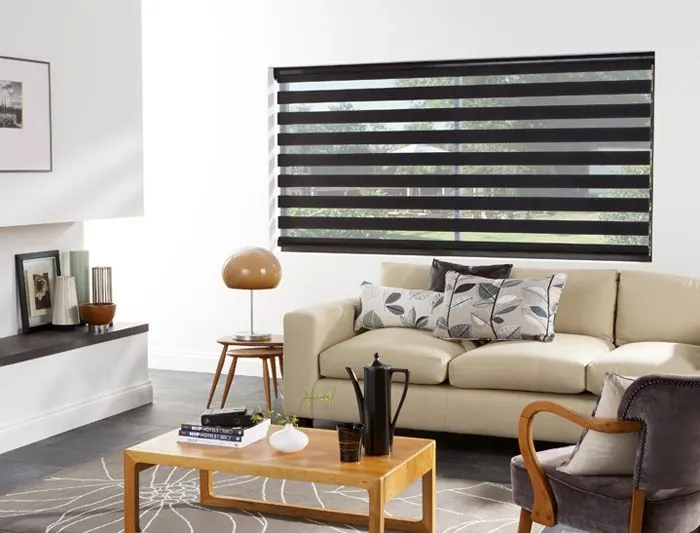 Store zébré noir sur mur blanc, canapé crème et table basse en bois